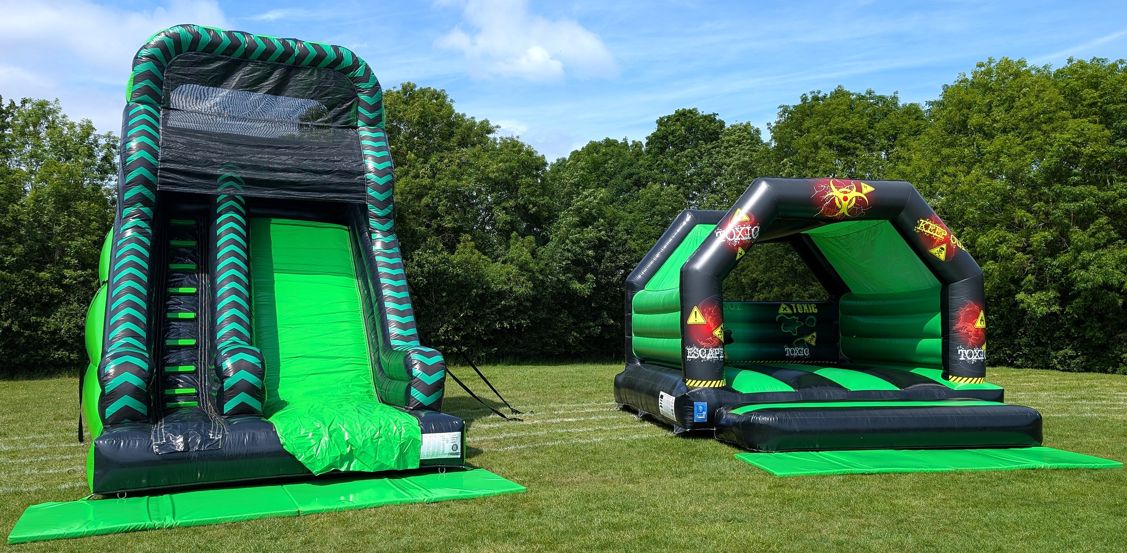 Toxic bouncy castle and green black 10ft inflatable slide package set up outdoors on grass