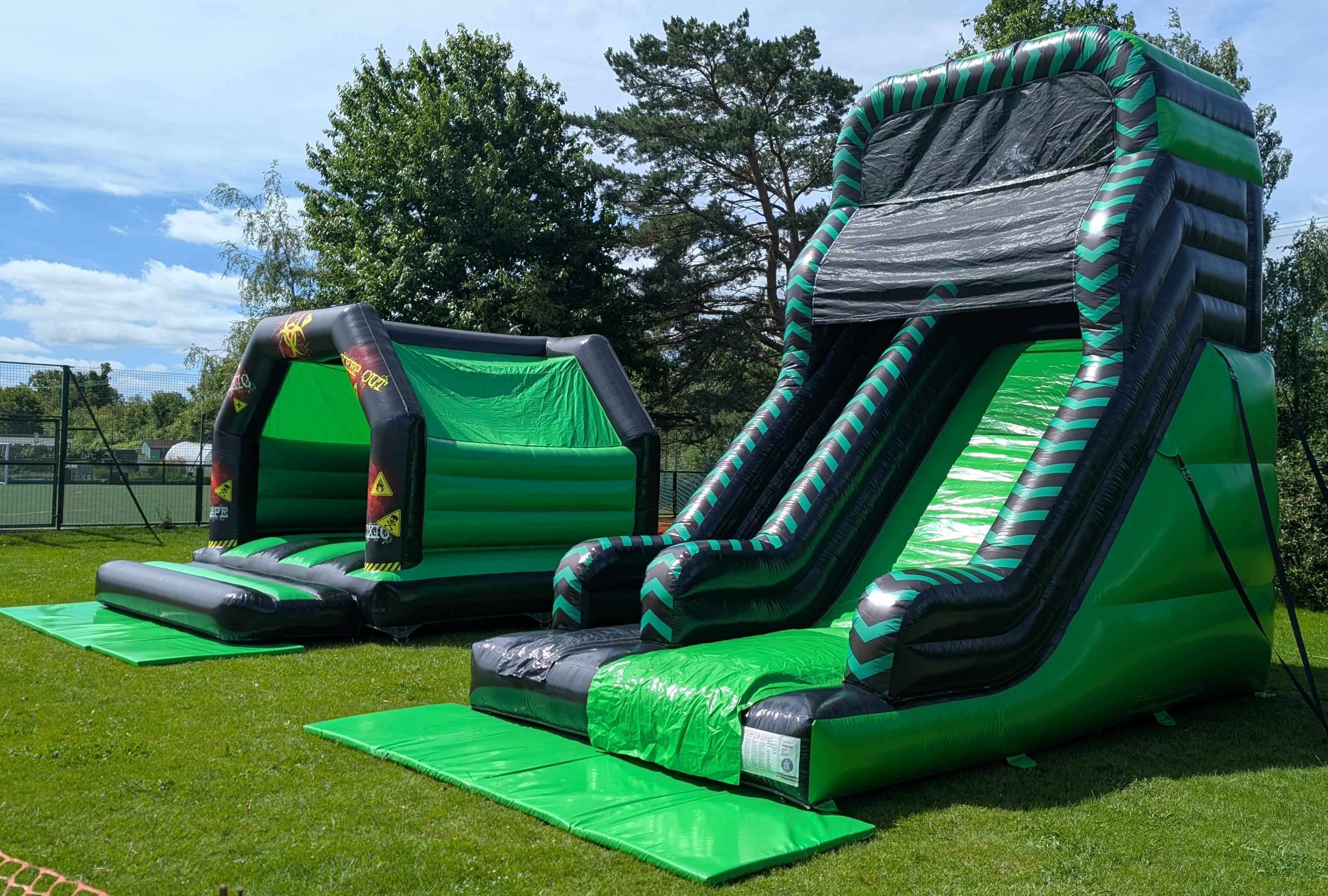Toxic bouncy castle and green black 10ft inflatable slide package set up outdoors on grass
