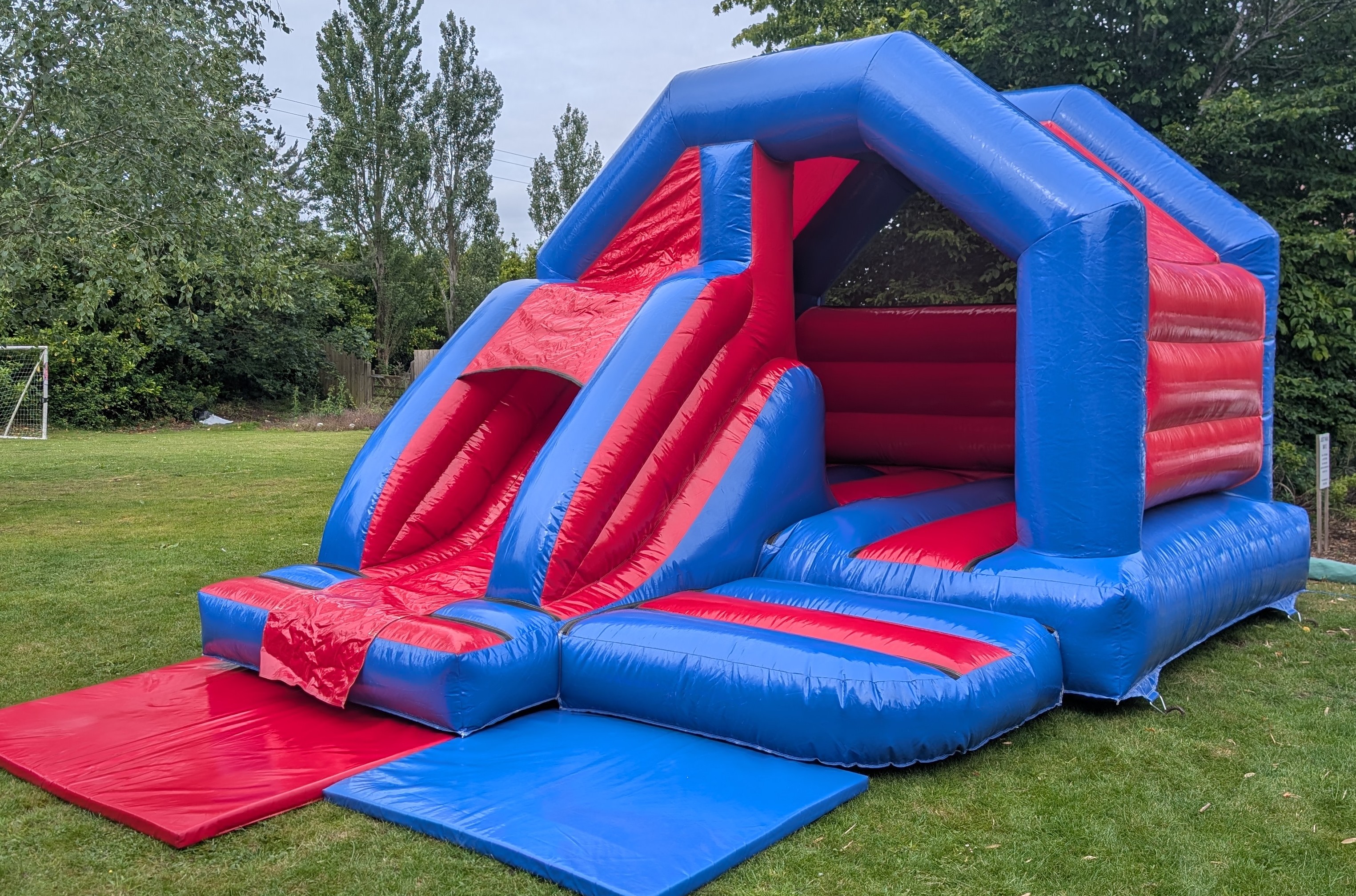 Red and Blue Bouncy Castle with Slide Hire Red and blue bouncy castle with slide set up in a garden in stansted